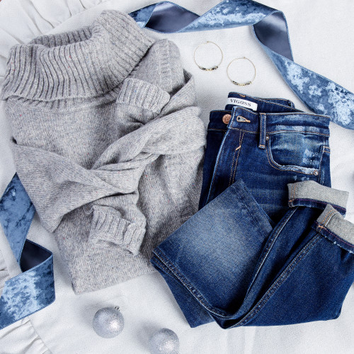 image of grey sweater, cuffed blue jeans, hoop earrings, holiday ornaments, and ribbon laying on a white background
