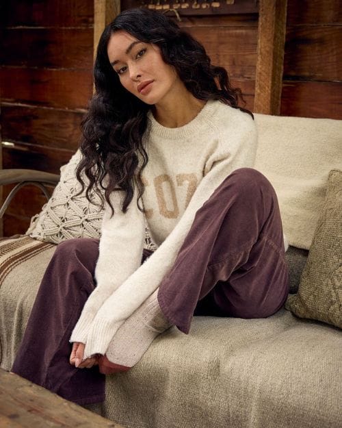 Brunette sitting on a couch in corduroy pants and a cozy graphic sweater.