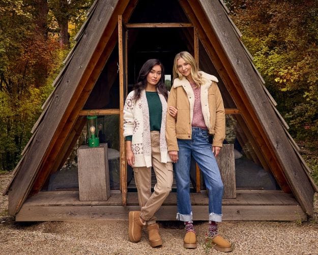 Two girls standing outside a cute cabin wearing cozy outfits from Wantable.