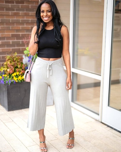 An influencer wearing a pair of gray sweater pants, a black tank, and strappy sandals. 