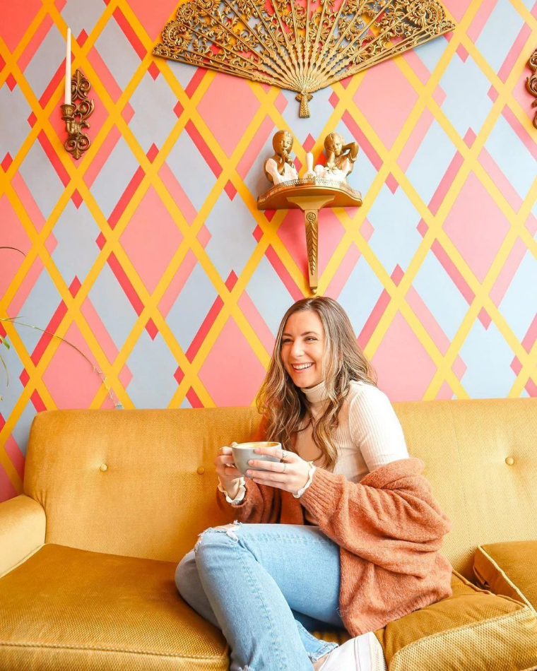 Woman sitting on a couch drinking coffee, one of the ways to love your body. @happilyeverdanielle