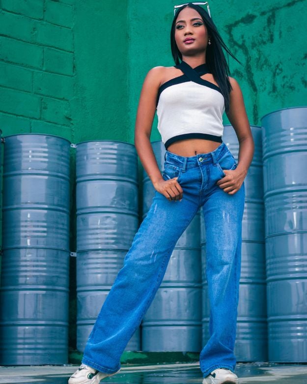 A woman with dark hair wearing a crop top and blue wide-leg jeans.