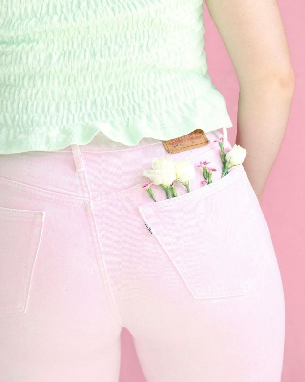 A model wearing a pair of pastel pink skinny jeans with flowers sticking out of her back pocket. 