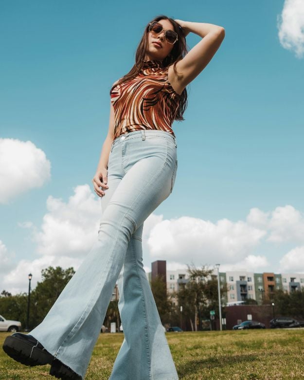 A girl wearing a retro outfit: a patterned tank top with light wash flared denim—one of the hottest 2025 denim trends. 