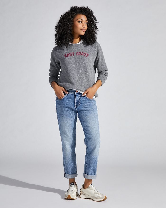 African American woman wearing light wash boyfriend jeans and a graphic sweatshirt that says "EAST COAST".