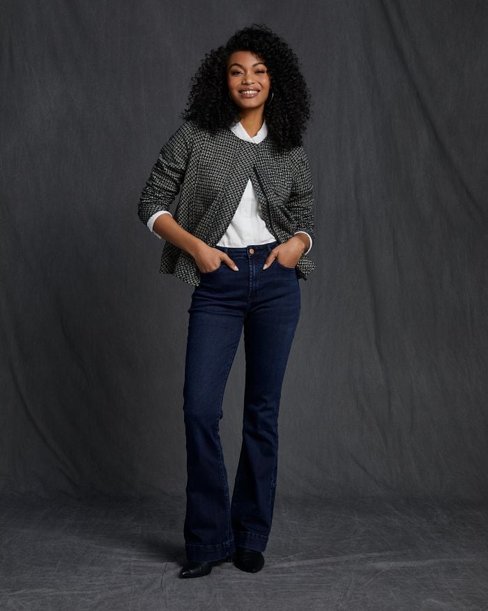 Smiling African American woman wearing dark wash flare jeans and a plaid jacket.