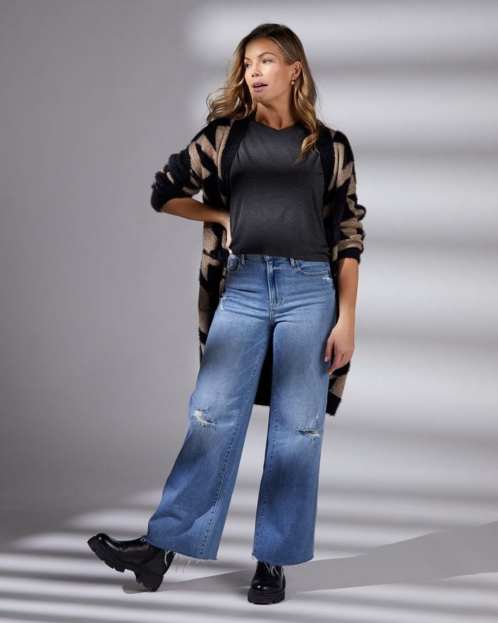 Blonde woman wearing medium wash wide leg jeans, a black tee, and a houndstooth cardigan.
