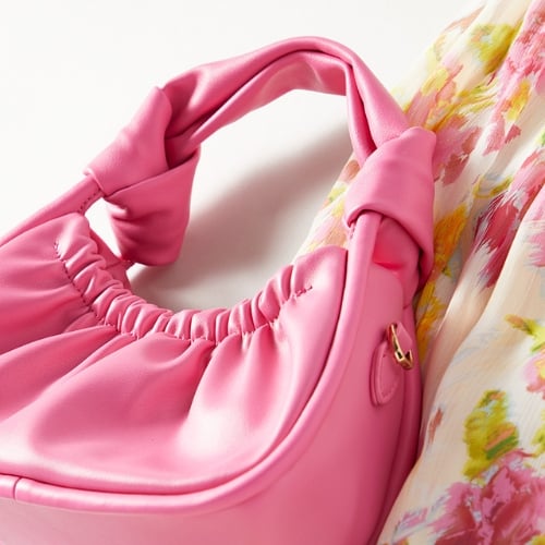 An up-close flat-lay photo showing a pink handbag next to a section of a white dress that has pink and yellow flowers printed on it. Shows an accessory to pair with spring dresses. 
