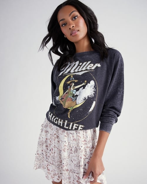 A photo of a Wantable model wearing a black Miller High Life sweatshirt layered over a printed ruffled mini dress. Shows styling spring dresses with a graphic sweatshirt.