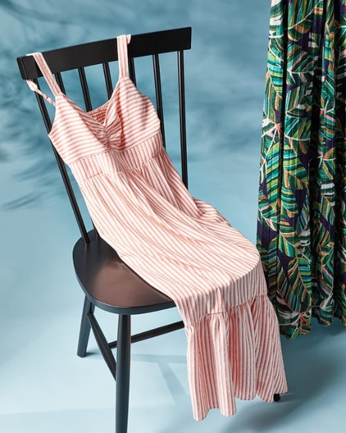 An up-close photo of a striped maxi dress laying across a black chair. 