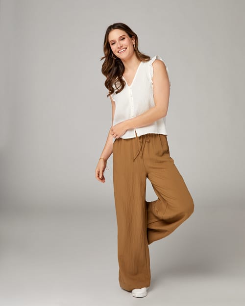 Smiling brunette wearing an easy outfit of a white blouse and wide leg gauze pants with a drawstring.