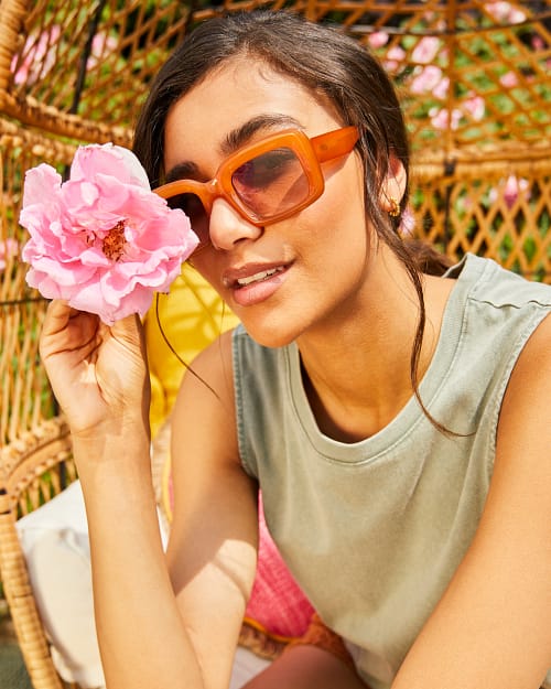 Brunette wearing sunglasses holding a flower in a spring setting.