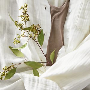 Close up of a white gauze button-down shirt holding a sprig of greenery.