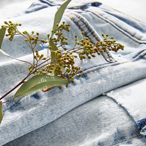 Close up of light wash jeans folded with a sprig of greenery.