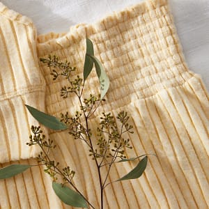Close up of a yellow ribbed pajama set and a sprig of greenery.