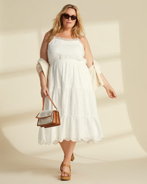 Plus size woman in a white eyelet midi length sundress, sunglasses, and a cardigan coming off her shoulders.
