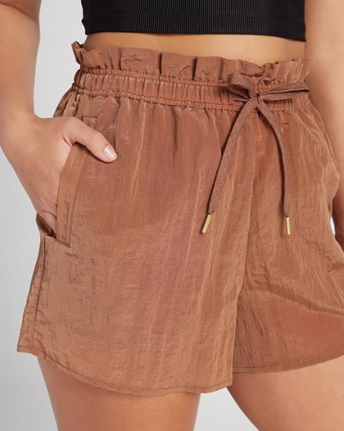 An up-close photo of a Wantable model wearing a pair of nylon paperbag shorts. One of her hands is in her pocket. 