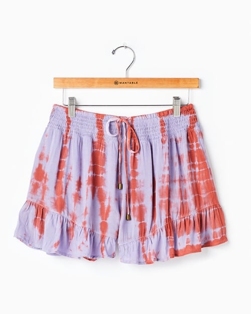 An up-close photo of a pair of tie-dyed ruffled shorts hung on a wooden Wantable hanger. 