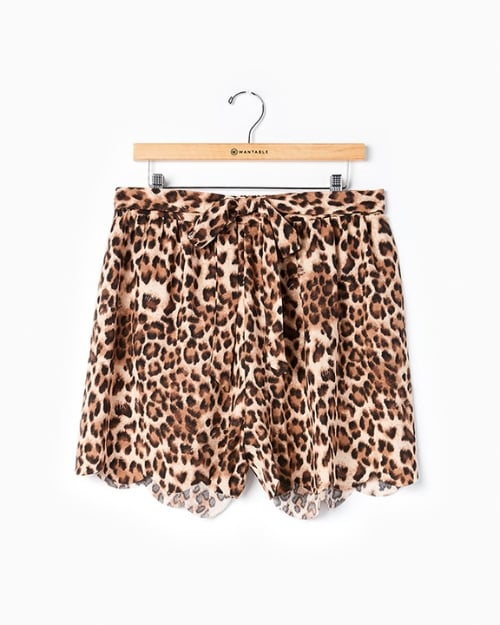 A photo of a pair of ruffled leopard print shorts hung on a wooden Wantable hanger in front of a white wall.