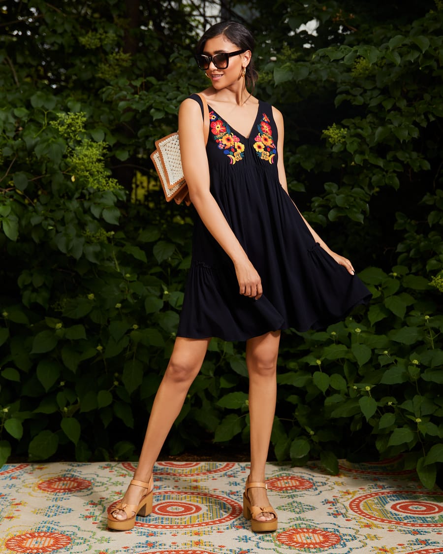 Smiling brunette at a backyard party wearing sunglasses and a flowy embroidered dress.