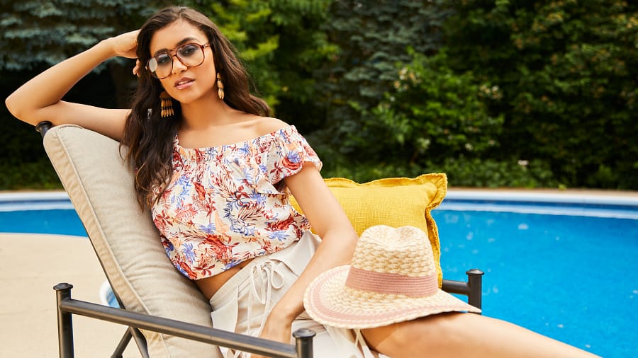 Brunette lounging on a pool chair during a backyard party wearing statement earrings, a floral blouse, and shorts.