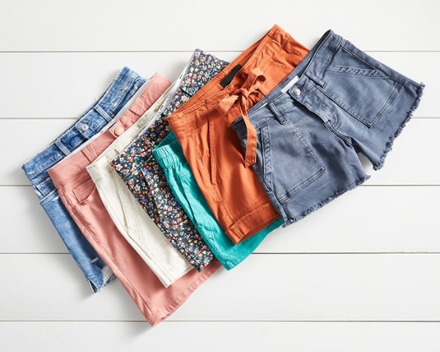 A photo of seven pairs of shorts stacked on top of each other on top of a white wooden slat background.