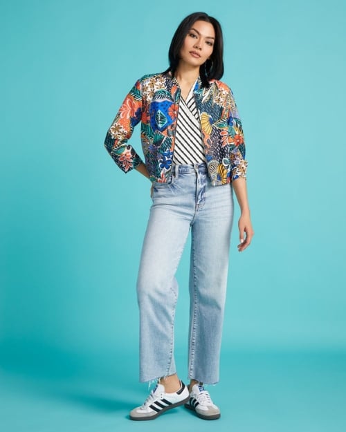 Model wearing a colorful, floral print bomber jacket and light-wash jeans paired with a striped asymmetrical tee. When learning how to style a bomber jacket, don't shy away from loud patterns. 