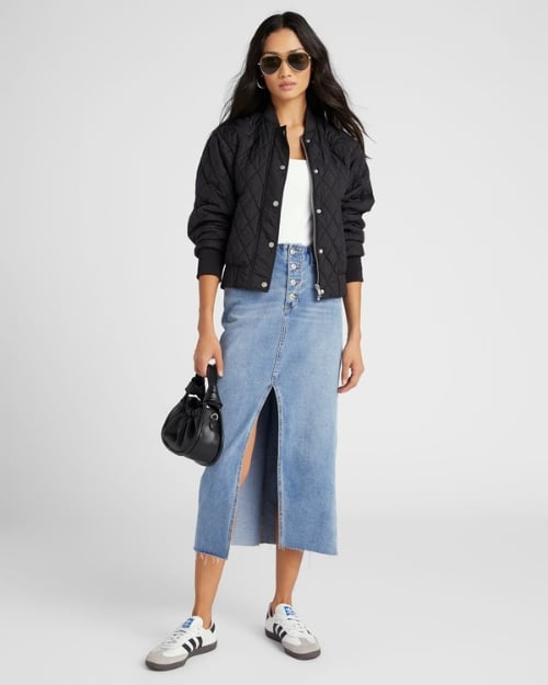 Model wearing a black quilted bomber paired with a simple white tee and denim midi skirt. 