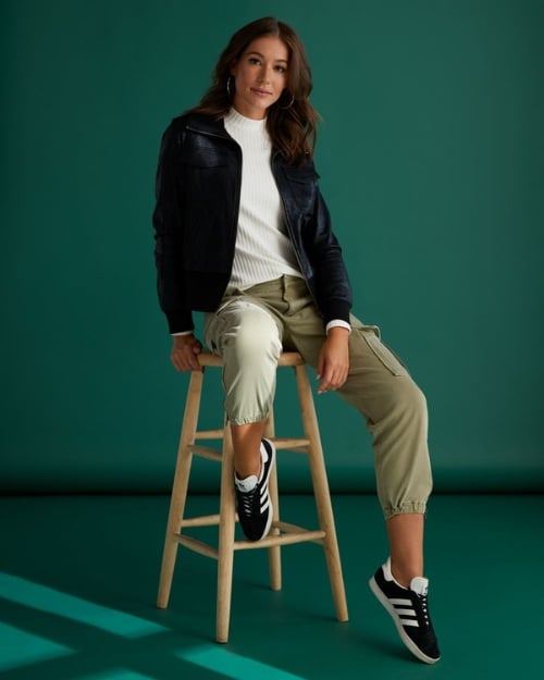 Model wearing olive green cargo pants, a white ribbed turtleneck, and a black leather bomber jacket. 