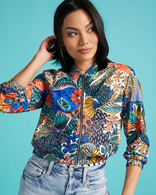Model wearing a colorful, floral print bomber jacket and light-wash jeans. 