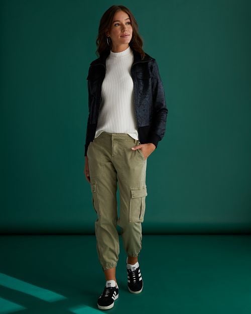 Model wearing a white turtleneck sweater, a black leather jacket, and classic green cargo pants.