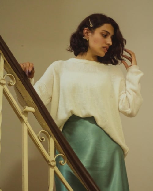 A woman with short brown hair wearing a green satin skirt and a white sweater.