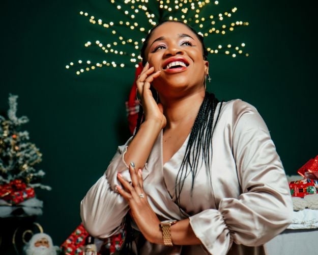 A woman in an off-white, long-sleeved satin blouse surrounded by Christmas decor.