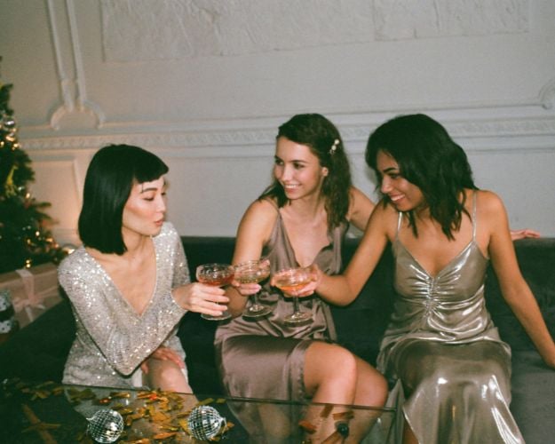 Three women dressed up for a holiday party sitting on a couch and having a champagne cheers.