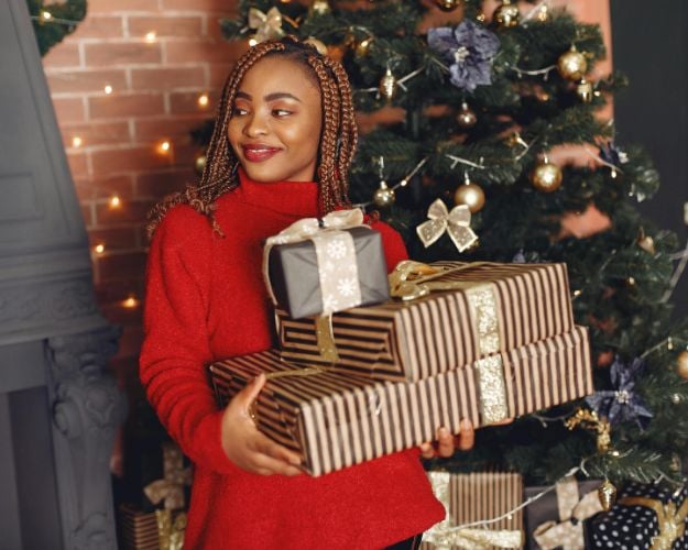 A woman in a red turtleneck sweater holding three Christmas presents. 