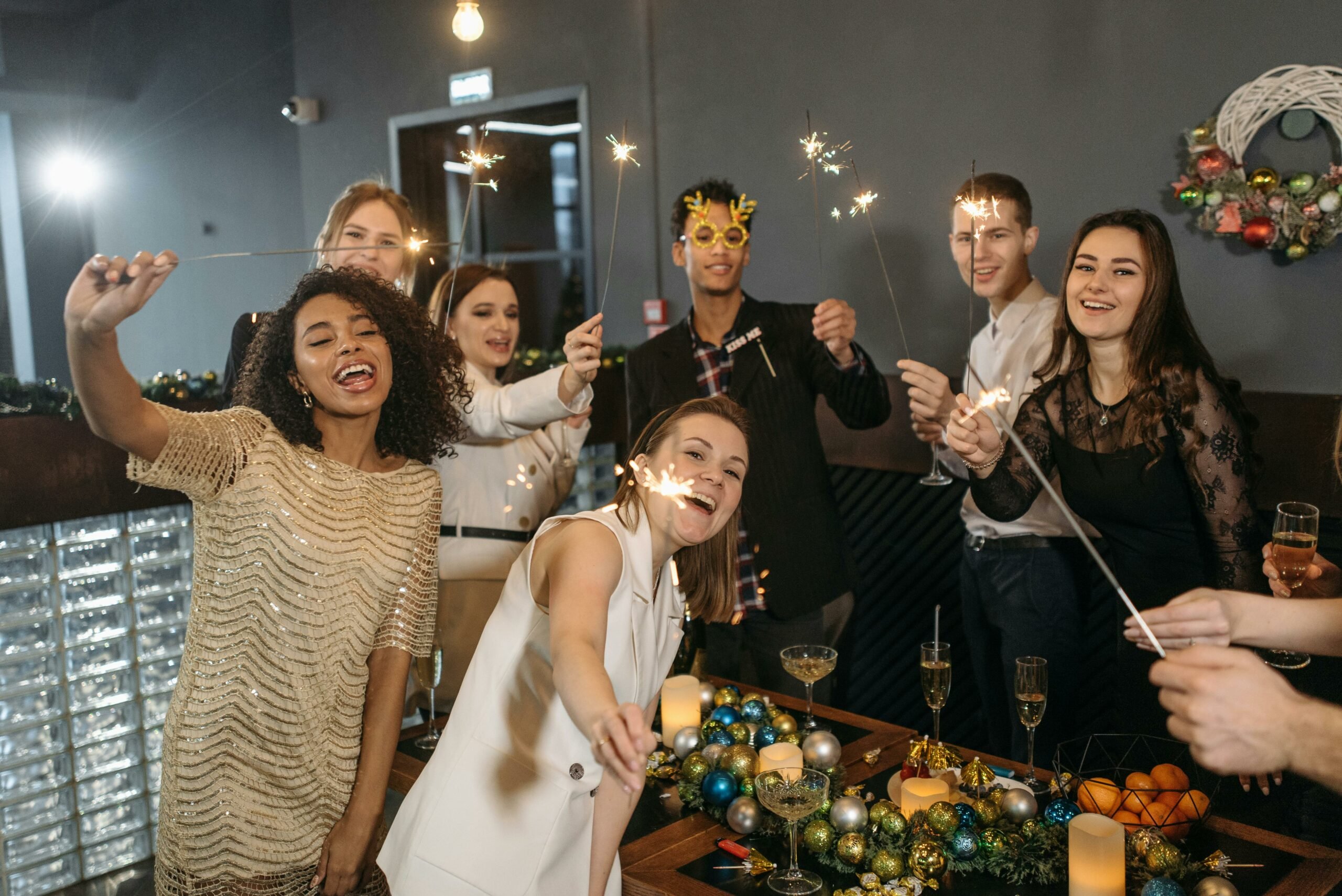 A group of coworkers holding sparklers and champagne at an office holiday party.